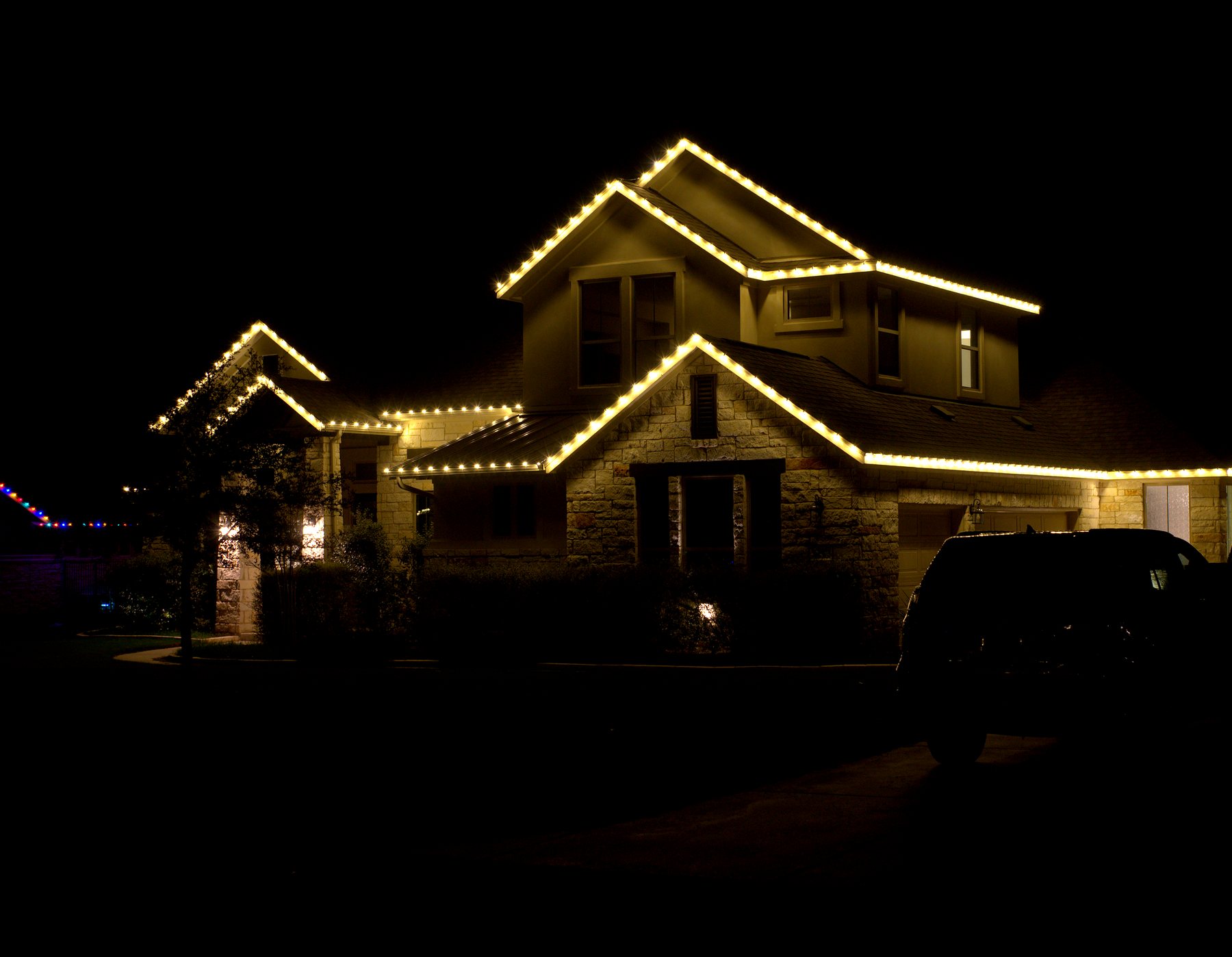 Two-story stone home with warm white lights outlining every roof peak and eave